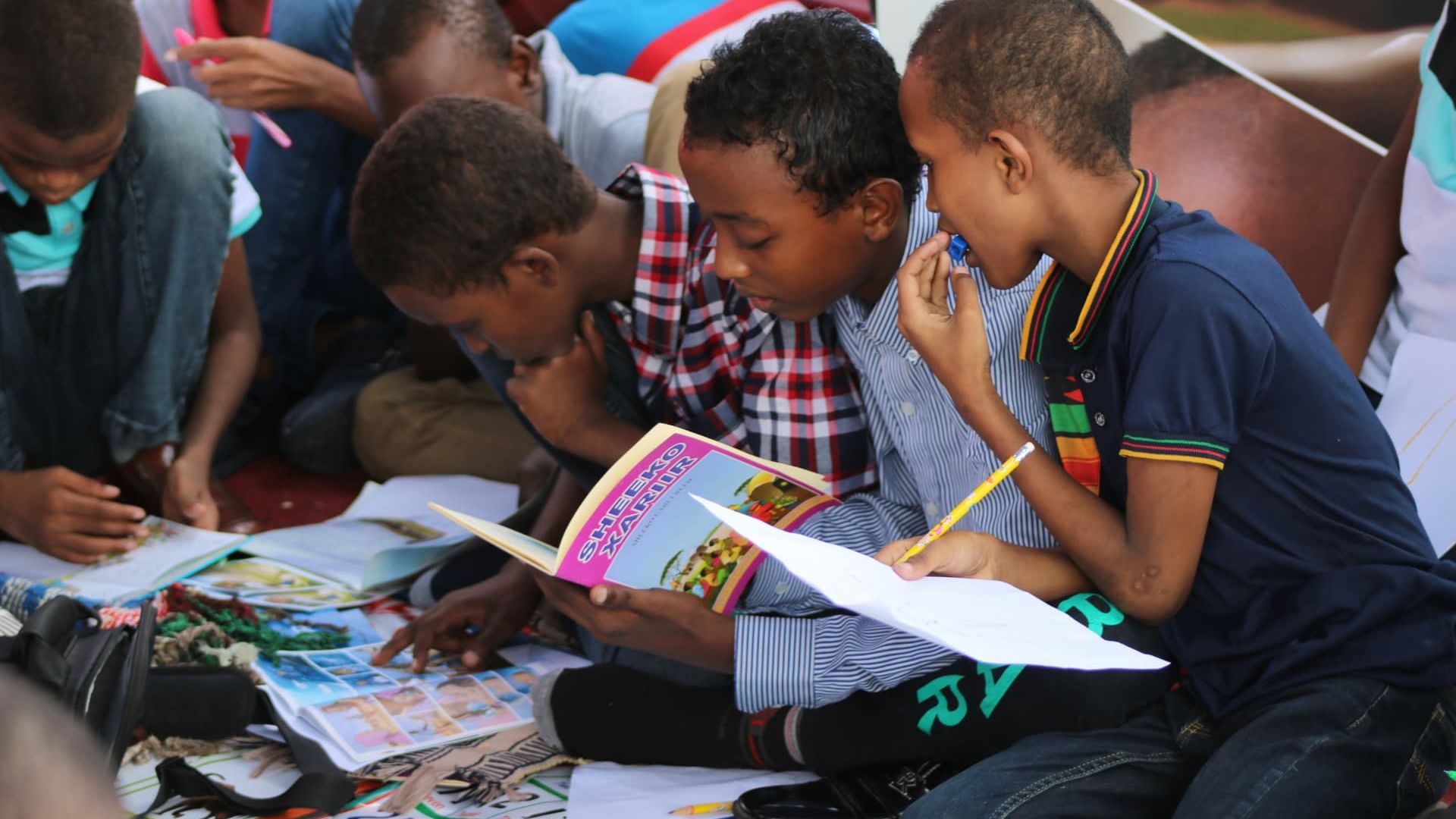 Children sitting together outdoors, reading storybooks at a community reading event